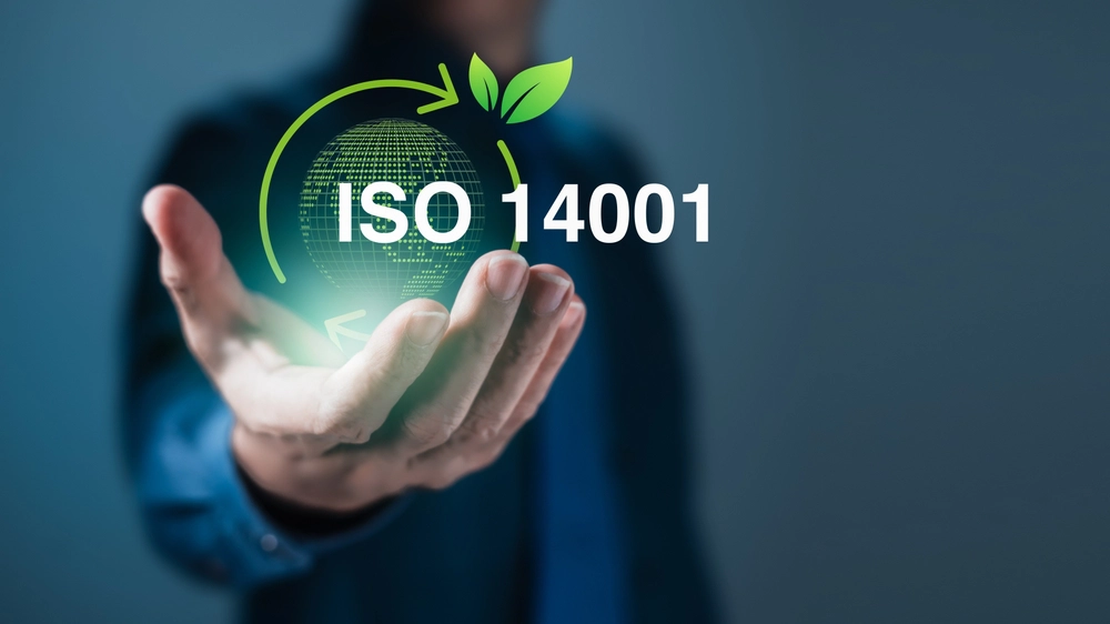 Hand hält digitalen Globus mit Schriftzug ISO 14001, grünem Kreislaufpfeil und Blättern als Symbol für Umweltmanagement