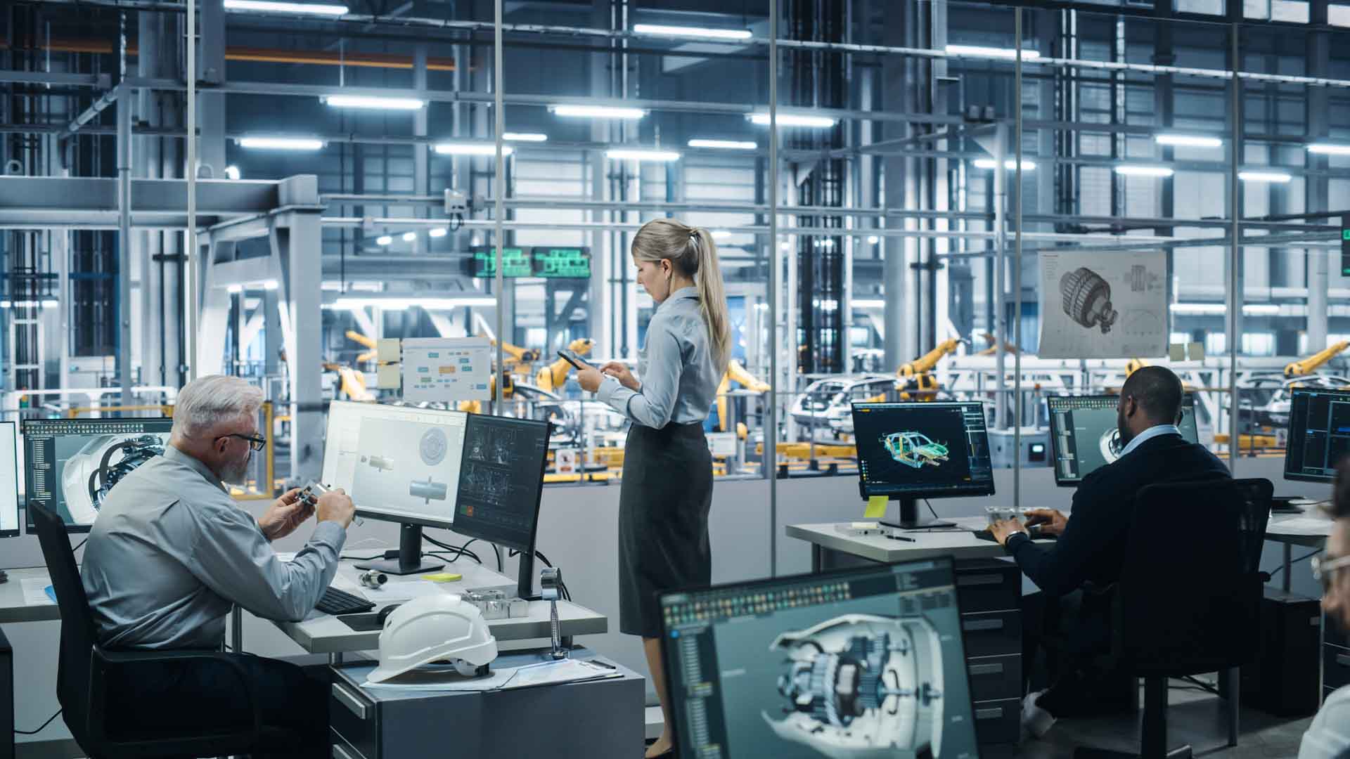 Ingenieurteam arbeitet an CAD-Modellen vor Glasscheibe mit Blick auf automatisierte Fahrzeugproduktion