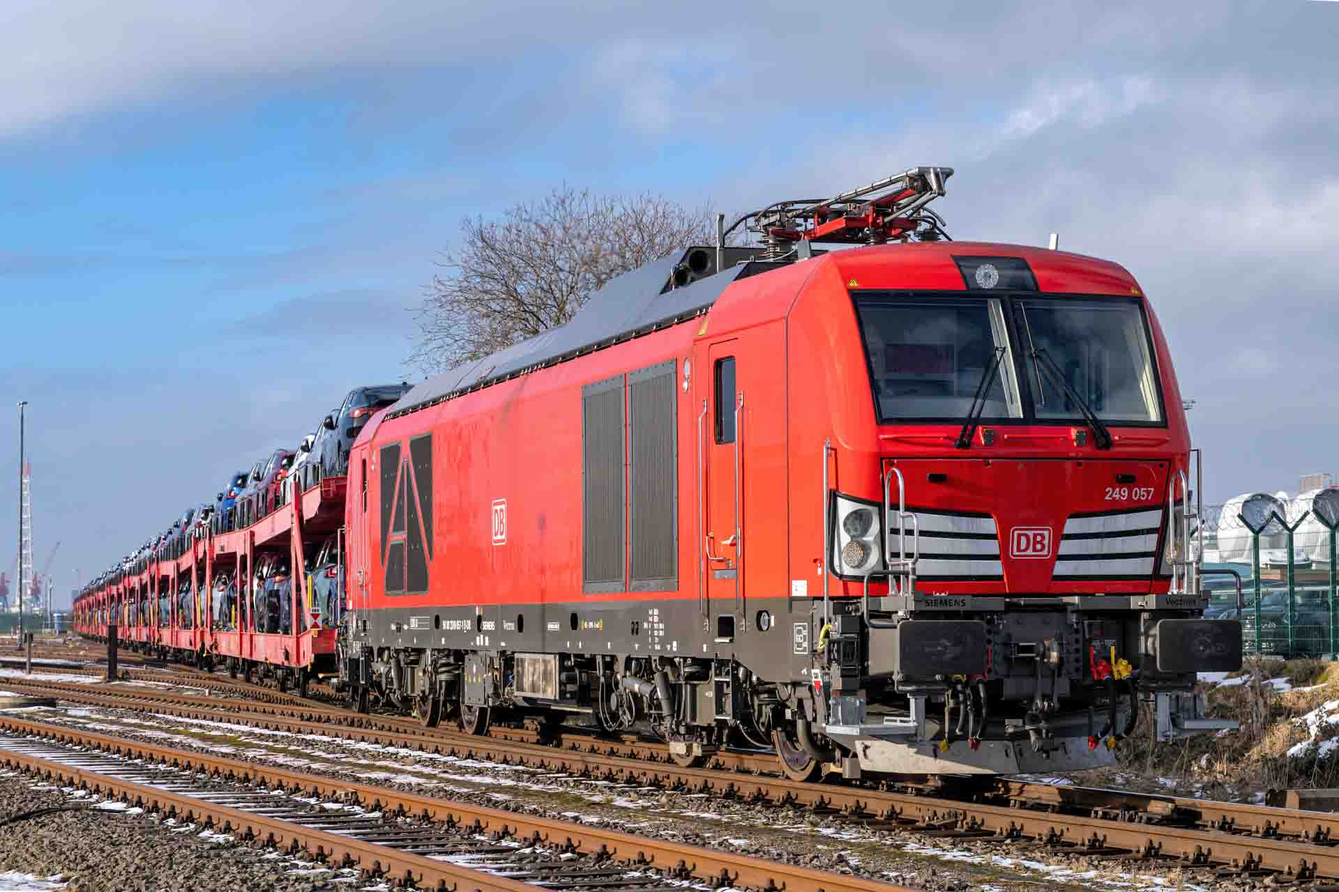 Rote DB-Lokomotive 249 057 zieht einen Autotransportzug auf freier Strecke bei blauem Himmel