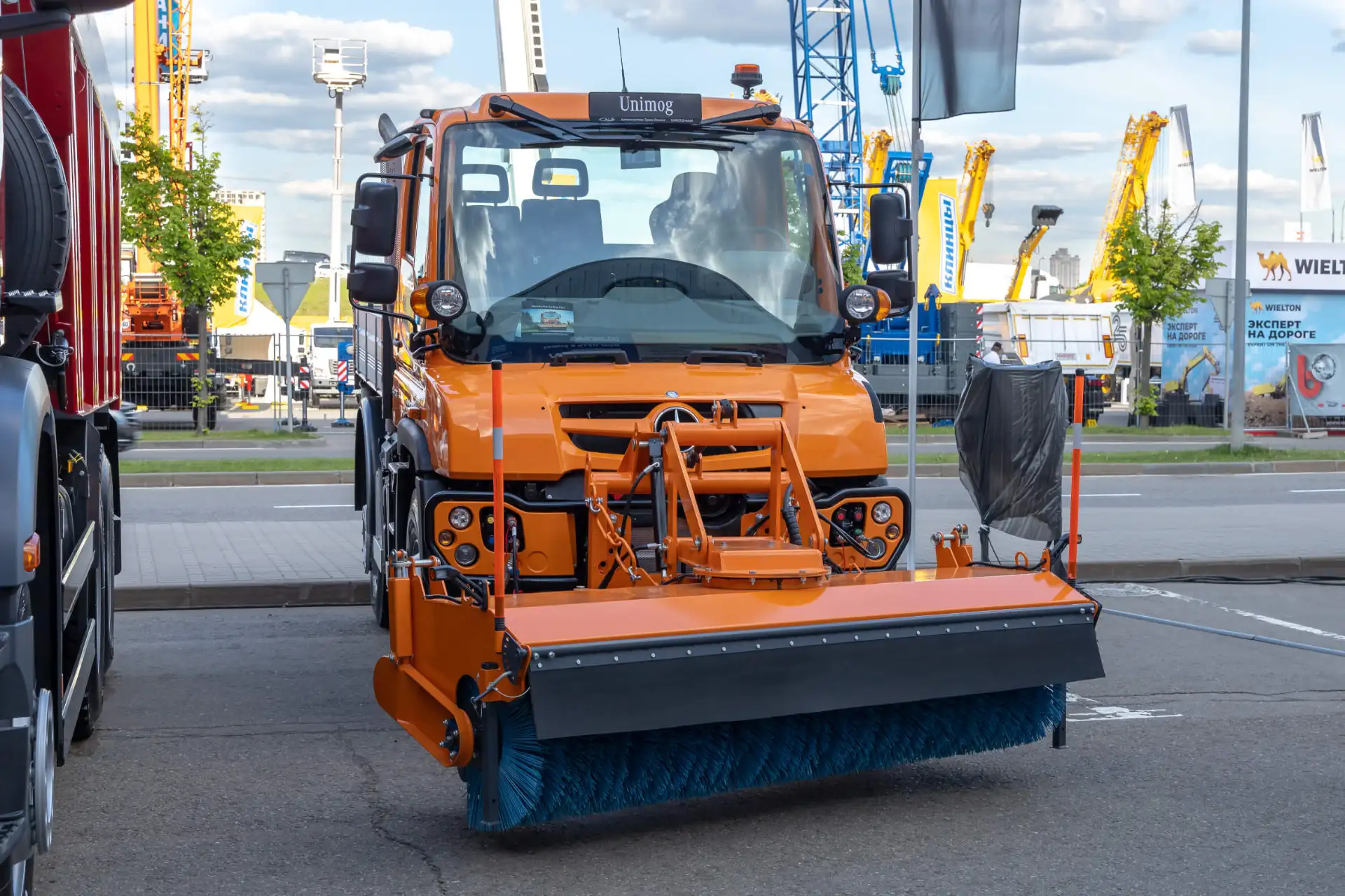 Orangefarbener Mercedes-Benz Unimog mit Frontbesen-Kehraufsatz auf einer Nutzfahrzeugmesse