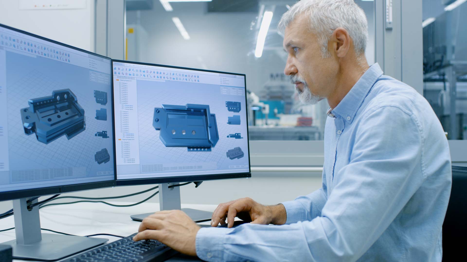 ngenieur mit grauem Bart arbeitet an CAD-3D-Bauteilmodellen auf zwei Monitoren im Technikbüro
