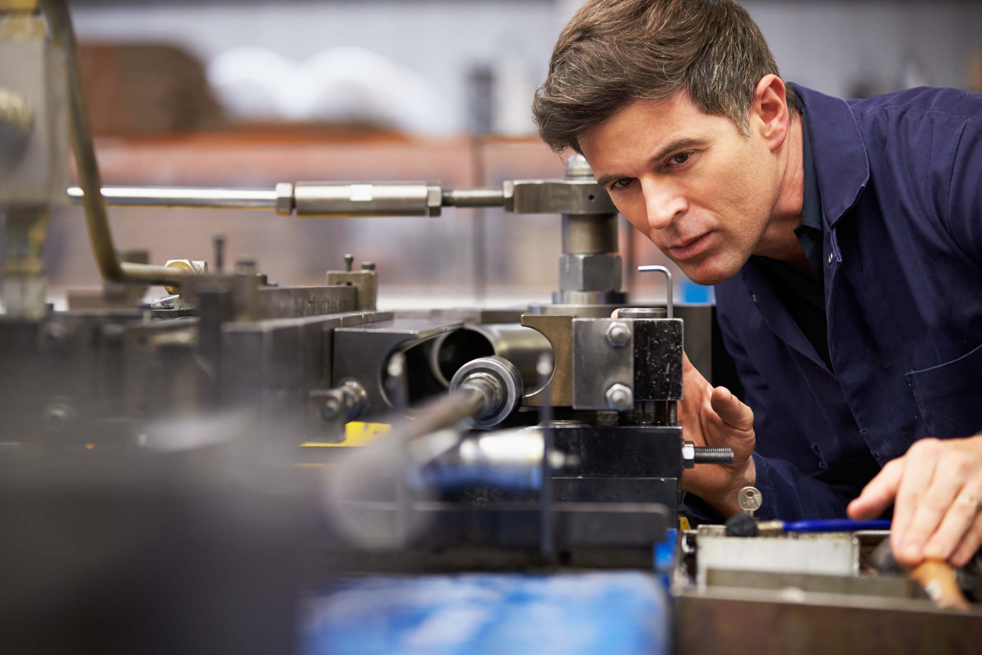 Techniker in blauem Arbeitshemd prüft konzentriert eine Drehmaschine in einer Metallwerkstatt
