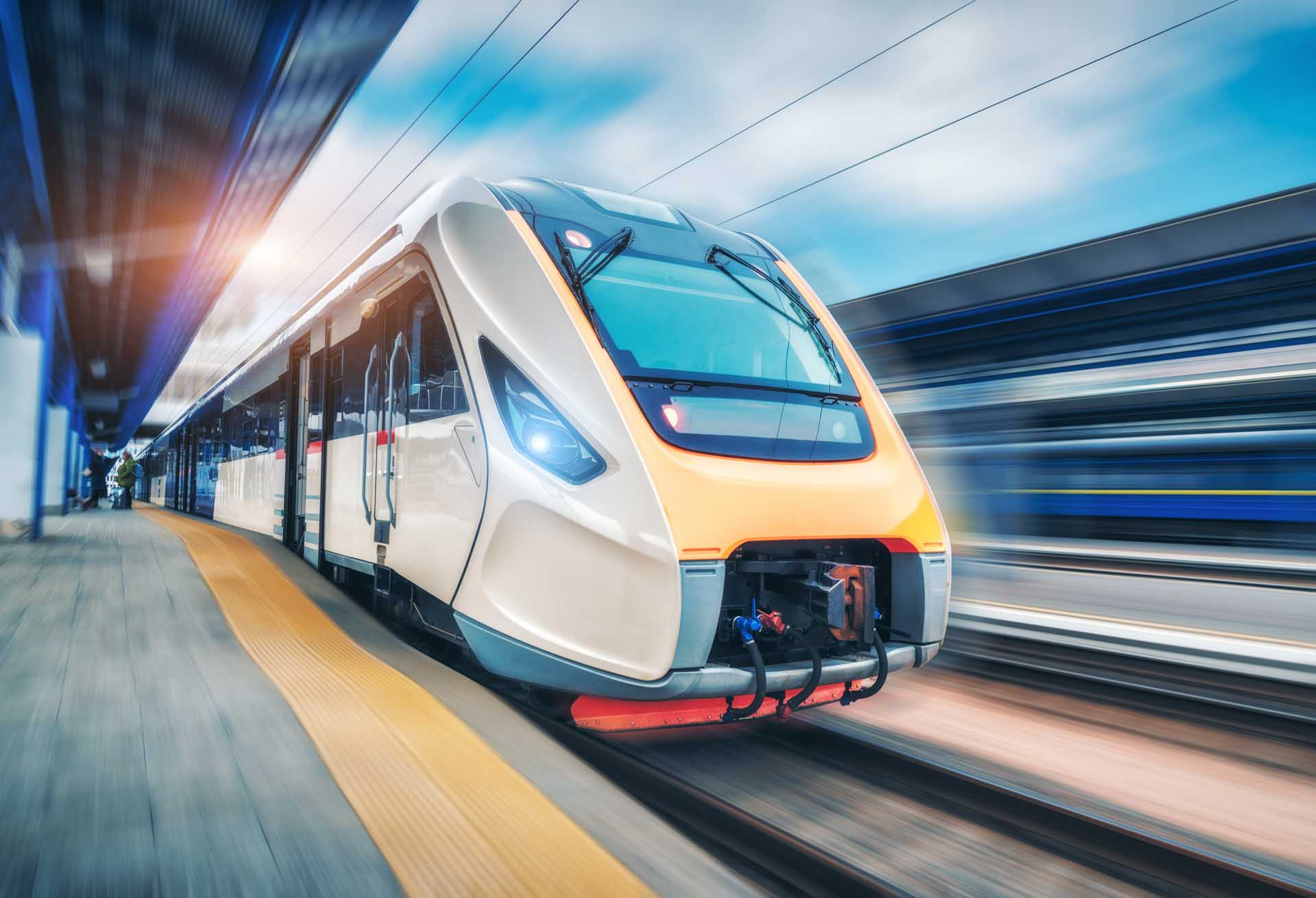 Moderner Hochgeschwindigkeitszug in Weiß-Orange fährt mit Bewegungsunschärfe an einem Bahnsteig vorbei